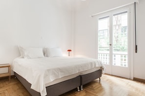A bedroom with a bed, a nightstand, and a window with a view of greenery.