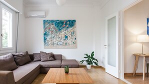 Ein modernes Wohnzimmer mit einer Eckcouch, einem Holztisch, einem großen abstrakten Gemälde, einer Topfpflanze und einer Lampe.