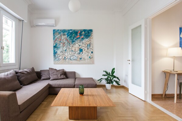 A modern living room with a sectional sofa, a wooden coffee table, a large abstract painting, a potted plant, and a lamp.
