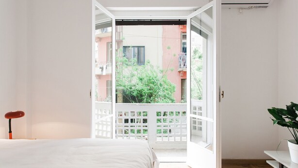 Ein Schlafzimmer mit einem Bett, einer weißen Tür, die auf einen Balkon führt, und einer Zimmerpflanze.