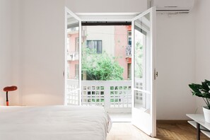 Un dormitorio con una cama, una puerta blanca que da a un balcón y una planta en maceta.