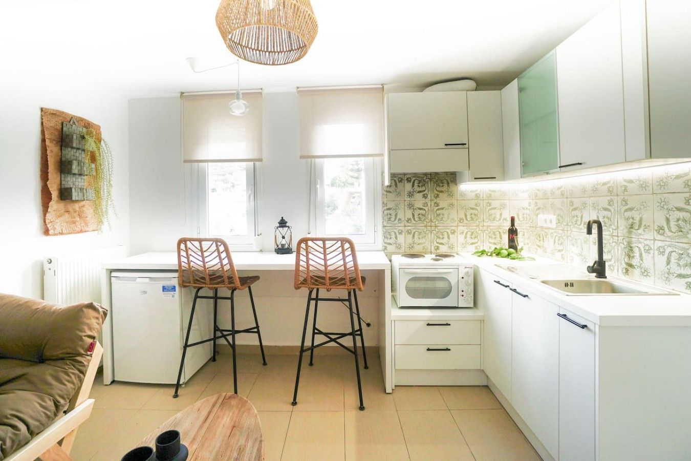 A compact kitchen with a refrigerator, microwave, and a sink. There are two bar stools and a small table.