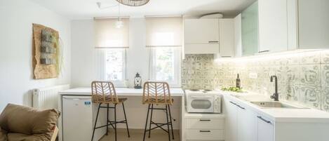 A compact kitchen with white cabinets, a built-in microwave, and a sink. There are two bar stools and a small dining table.