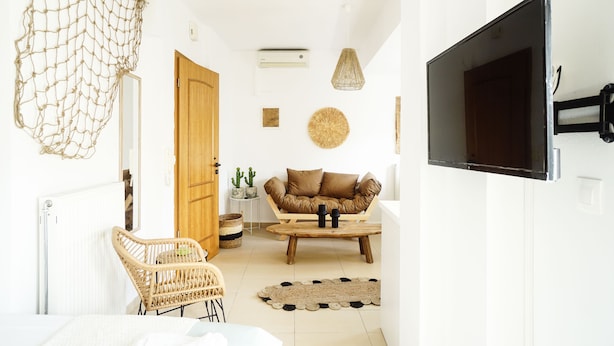Een woonkamer met een bank, een salontafel, een aan de muur bevestigde televisie, een rieten fauteuil en een hangende netdecoratie.