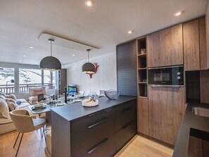 A modern kitchen with wooden cabinets, a built-in microwave, and a dining area with a view of the outdoors.