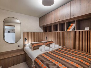 Un dormitorio con cama, espejo, cabecera de madera y estante empotrado con libros.