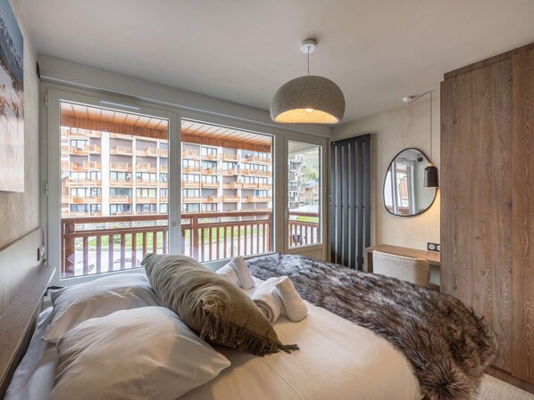 A bedroom with a large bed, a wooden headboard, a round mirror, and a view of a building through a sliding door.