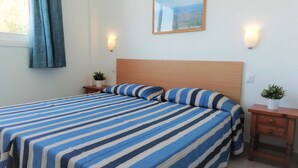 Une chambre d’hôtel avec un grand lit, deux tables de chevet, une commode, une fenêtre avec des rideaux et un tableau encadré au mur.