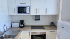 Une cuisine moderne avec des meubles blancs, un four à micro-ondes encastré, un grille-pain, une machine à café, un lave-linge et un réfrigérateur.