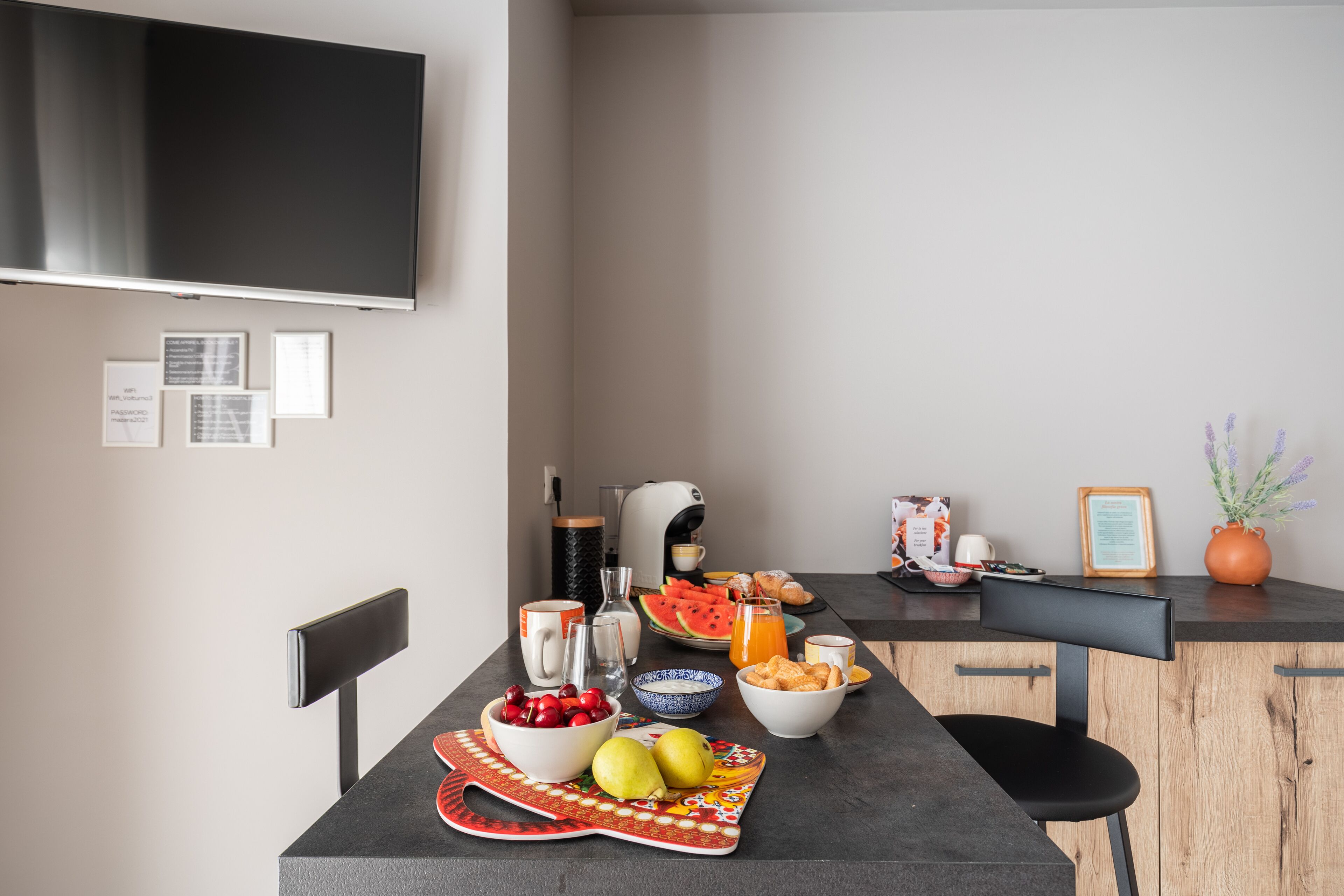 Una cocina moderna con una mesa de desayuno dispuesta, que incluye frutas, bollería y una cafetera.