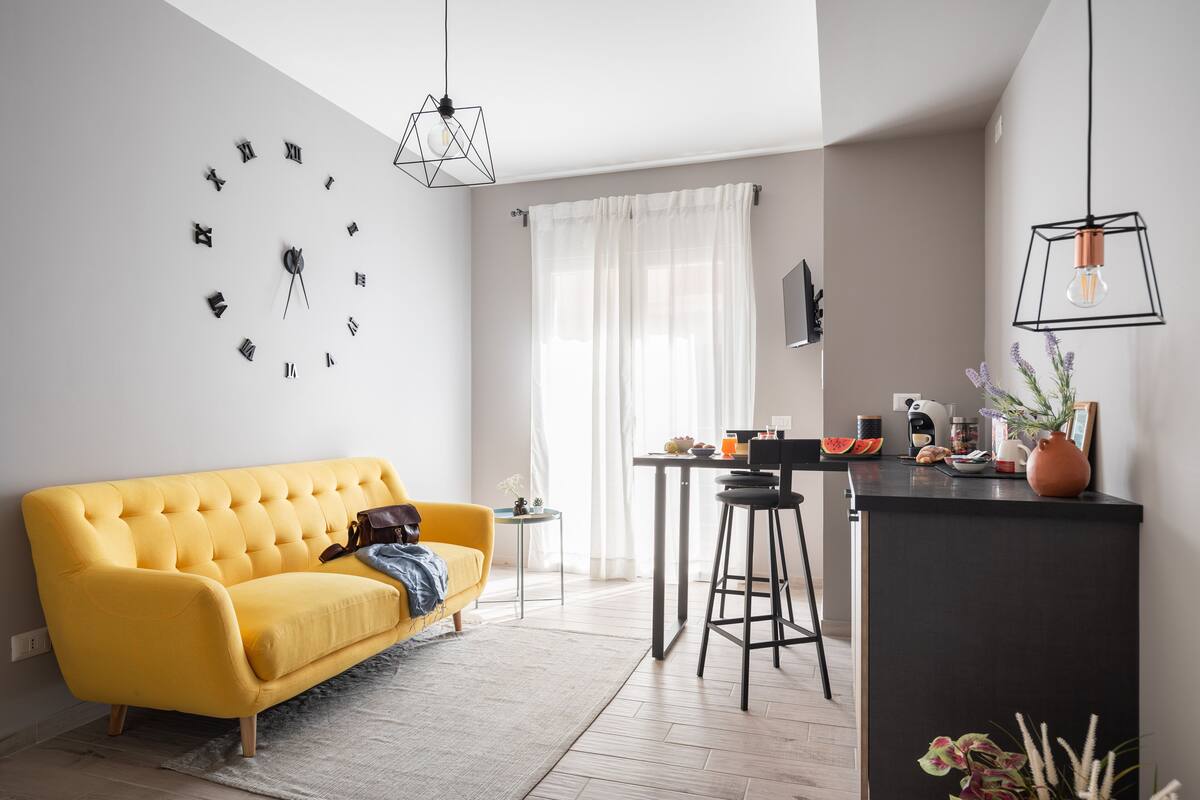 Un salon moderne avec un canapé jaune, un coin repas doté d’un bar et une grande horloge murale.