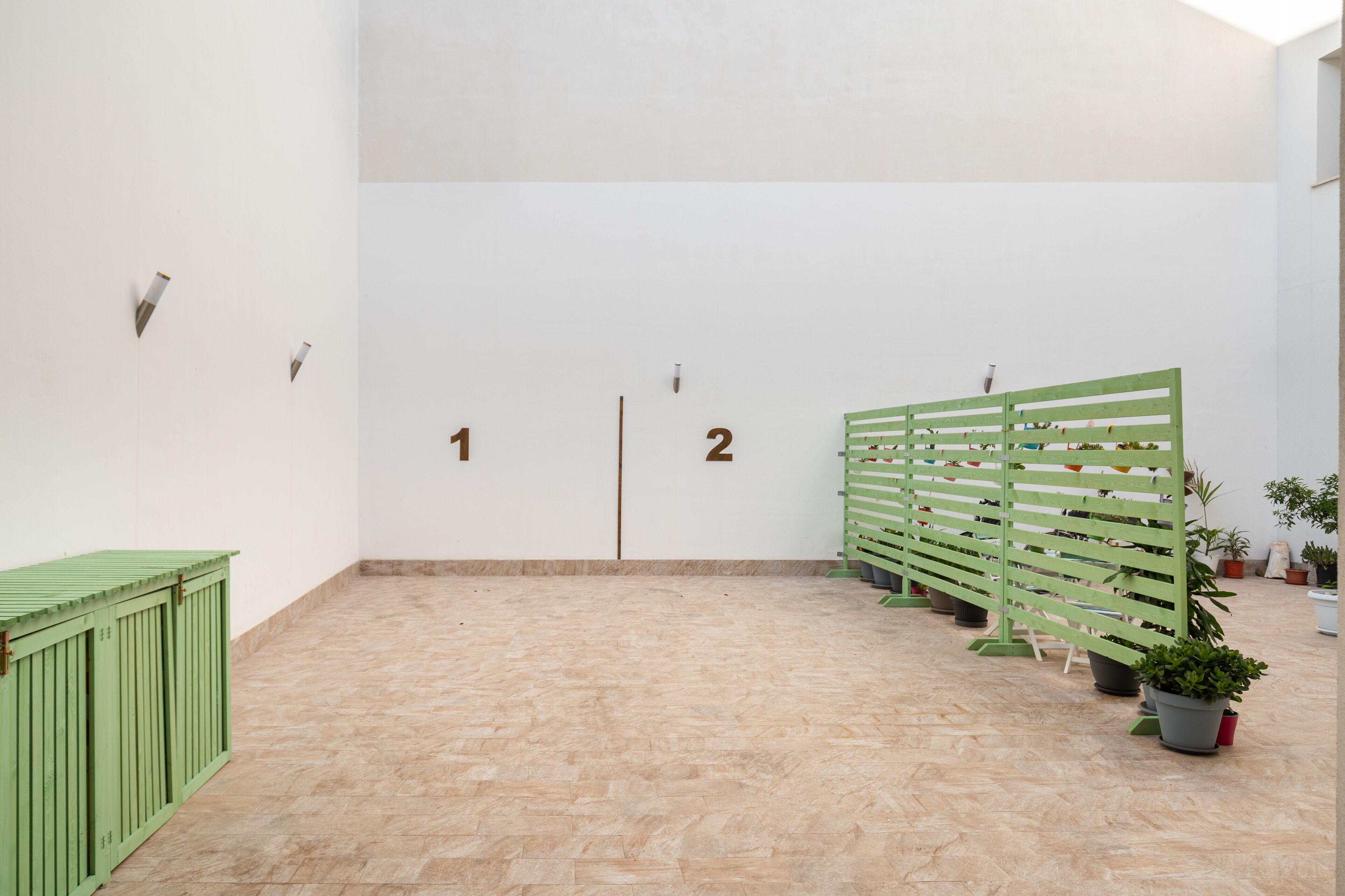 Una habitación minimalista con puertas numeradas, un separador verde y plantas en macetas.