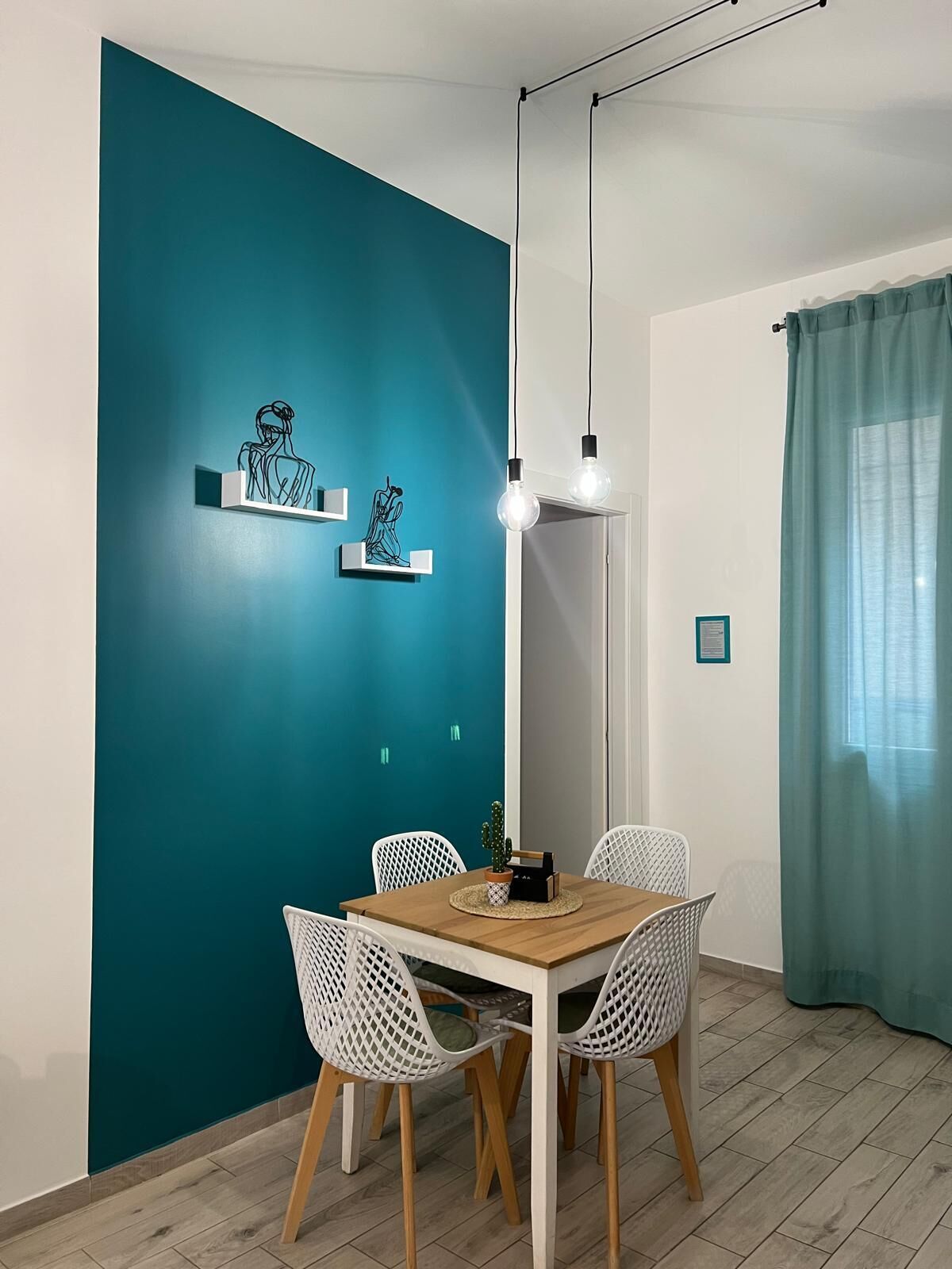 A dining area with a teal accent wall, white chairs, a wooden table, and pendant lighting.