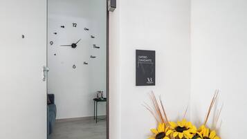 A room with a wall clock, a sign reading "SATIRO DANCANTE V3", and a vase with sunflowers.