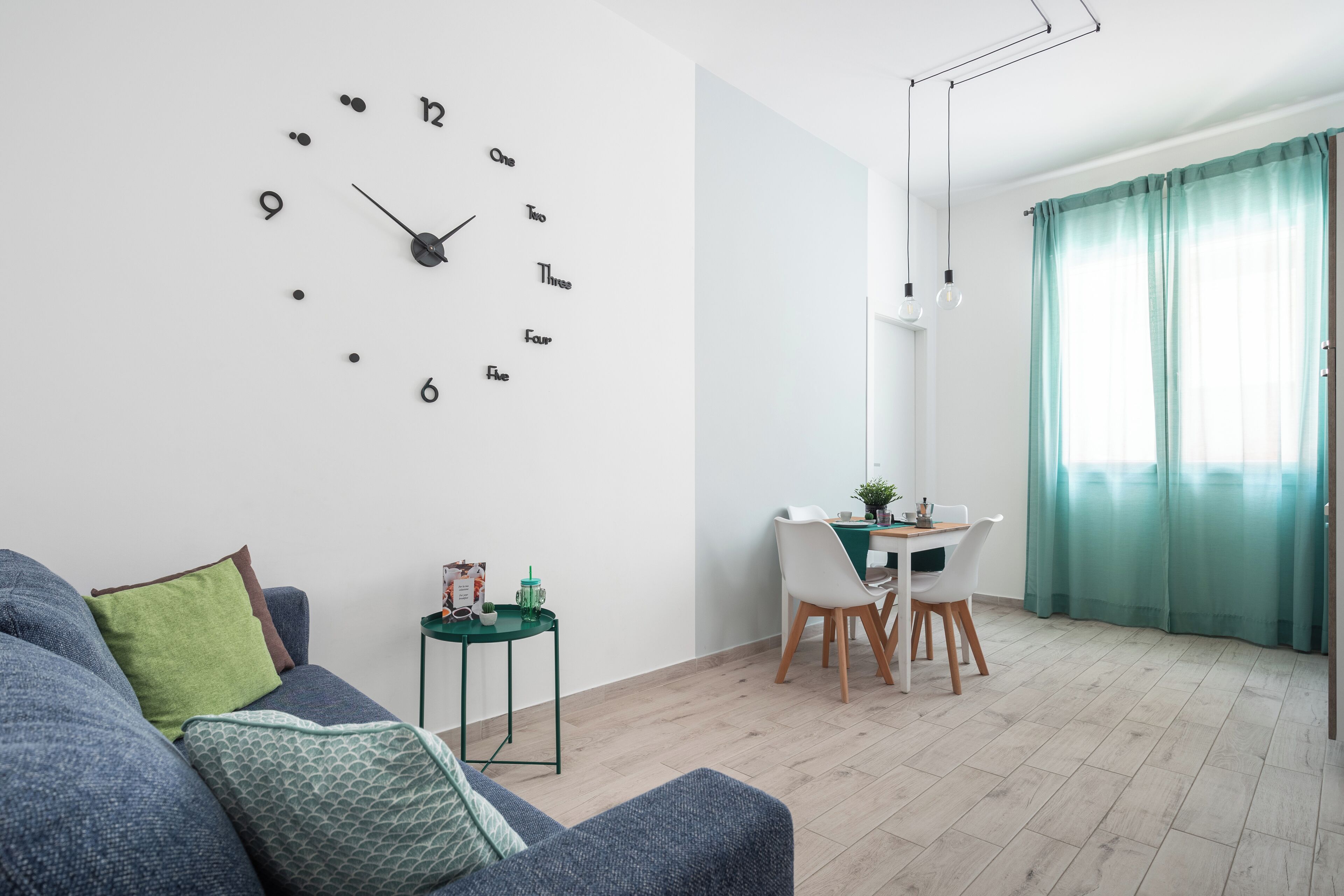 Un salon moderne avec une horloge murale, un coin repas avec une table et des chaises, et un canapé avec des coussins.