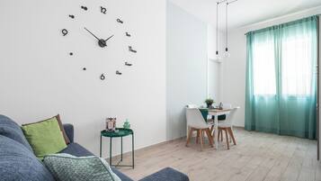 Un salon moderne avec une horloge murale, un coin repas avec une table et des chaises, et un canapé avec des coussins.