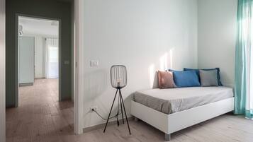 Ett sovrum med en vit säng, en golvlampa och utsikt över en hall.