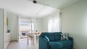Un soggiorno moderno con un divano color petrolio, un'area pranzo con tavolo bianco e una zona cucina con forno a microonde.