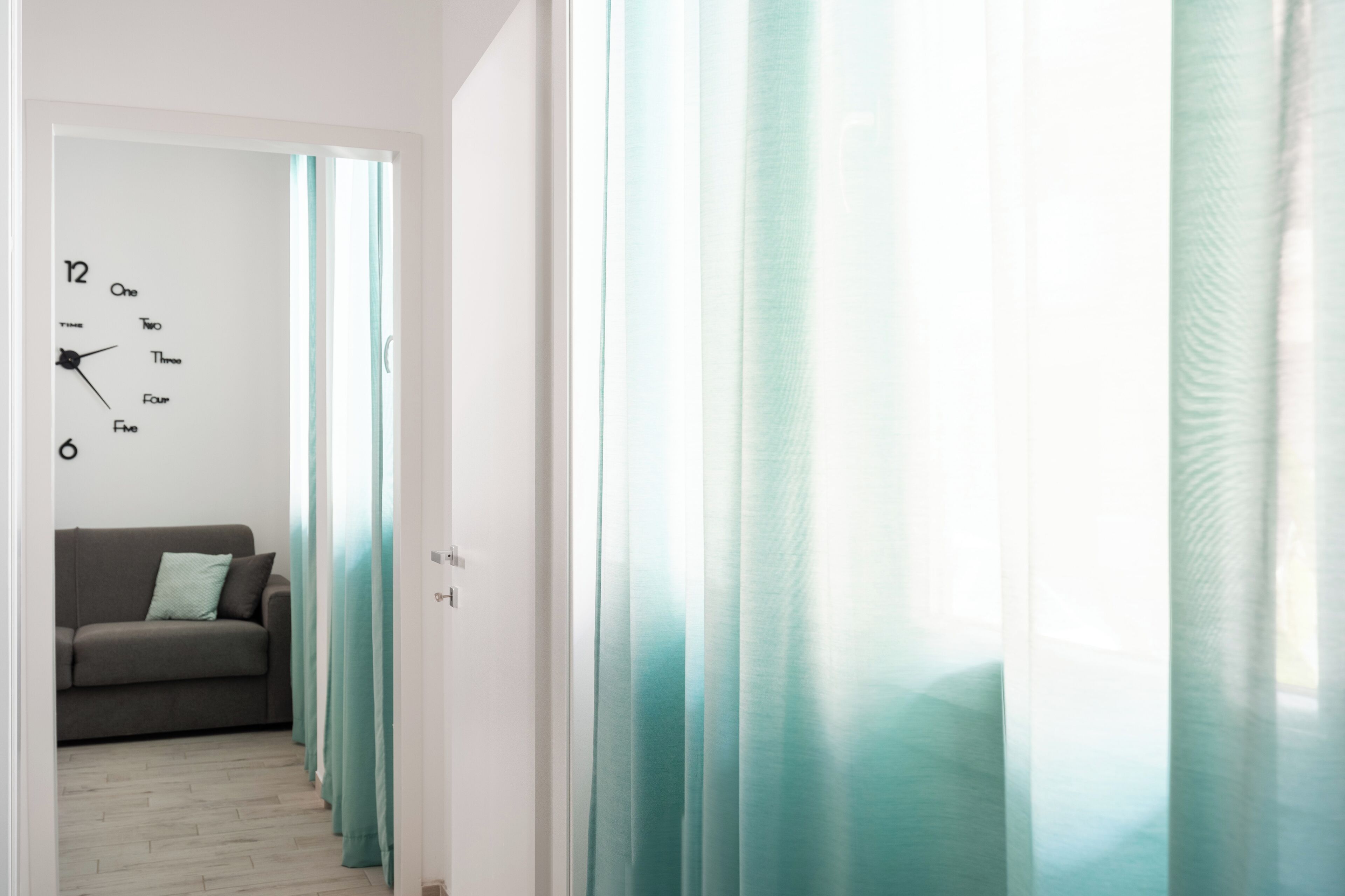 Un pasillo con un reloj en la pared, un sofá y cortinas color turquesa.