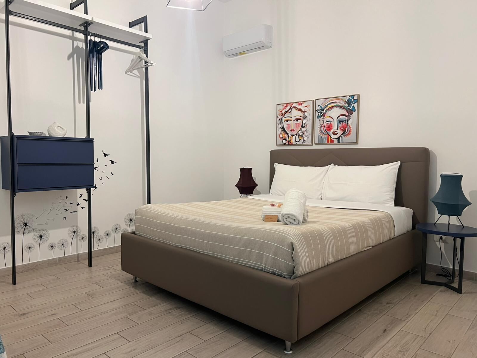 Quarto com cama, cómoda, candeeiro e duas pinturas na parede.