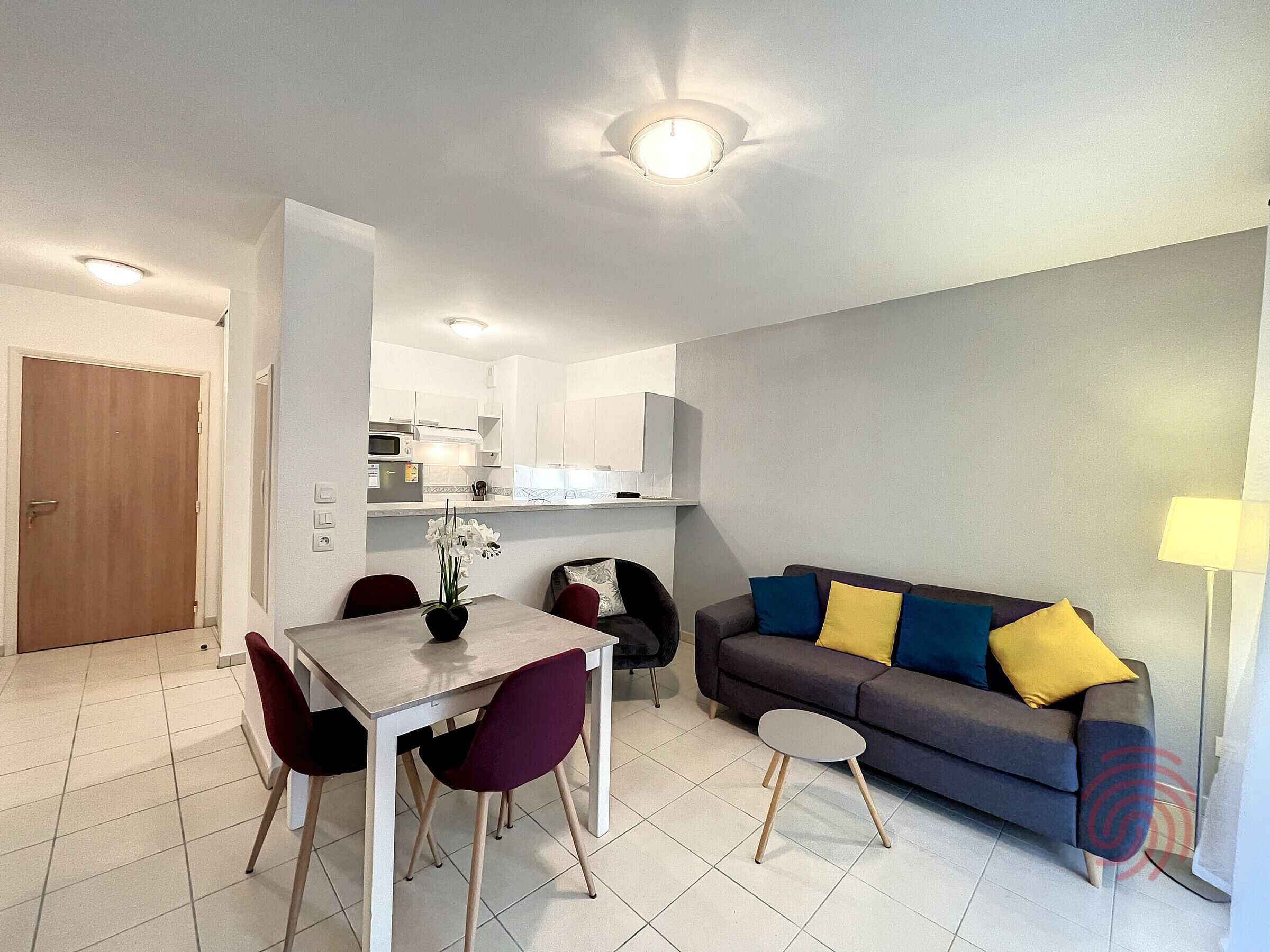 A modern living room with a dining area, a sofa with colorful cushions, and a small side table.
