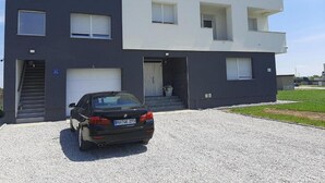 Una casa moderna de dos pisos amb façana negre i blanca, un carrer d'accés i un cotxe negre aparcat.