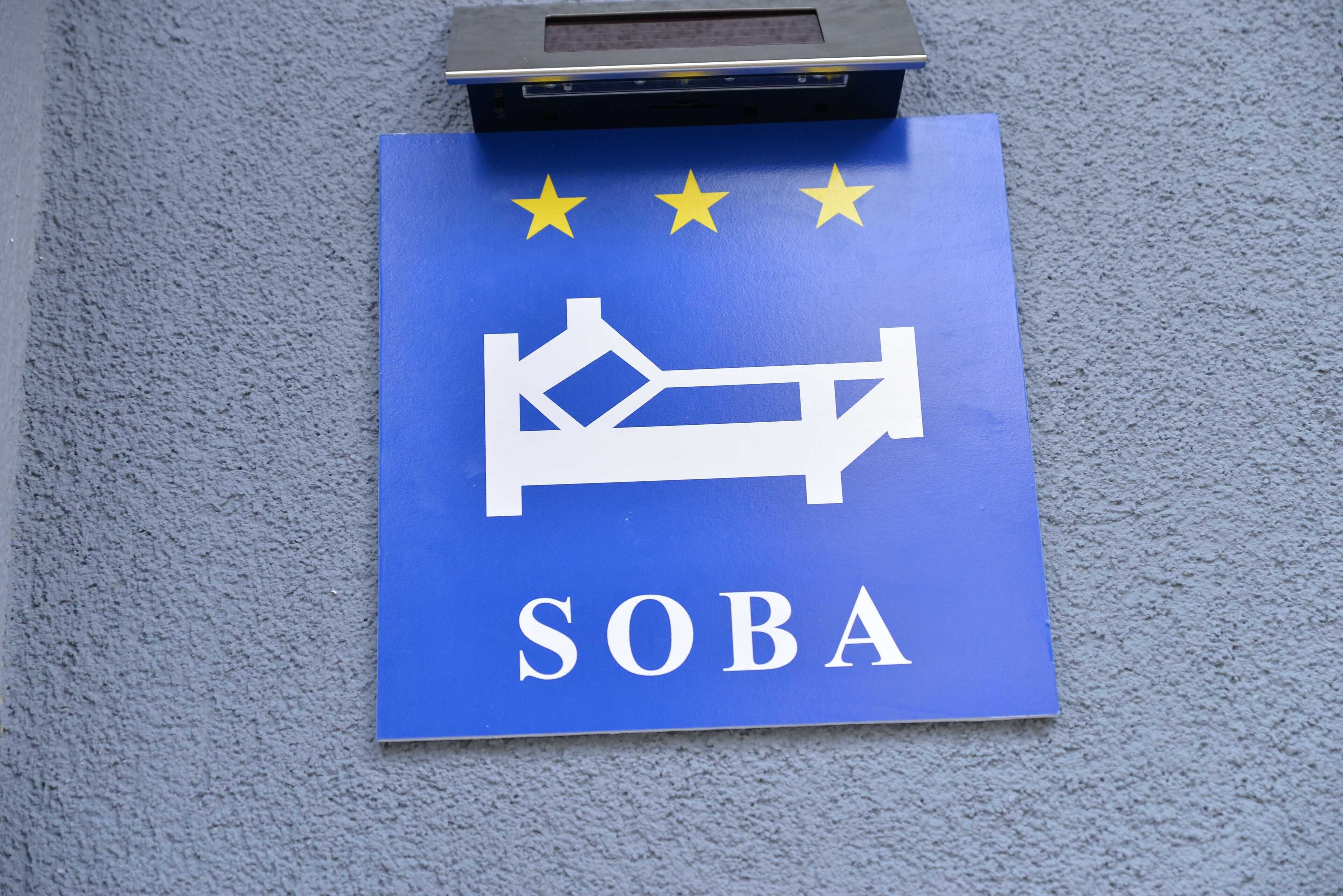A blue sign with a bed icon and the word "SOBA" on a textured wall.