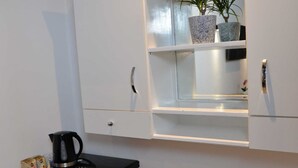 Eine kleine Küchenzeile mit schwarzer Arbeitsplatte, einem weißen Mini-Kühlschrank, einer Kaffeemaschine und einem Blumentopf auf einem Regal.