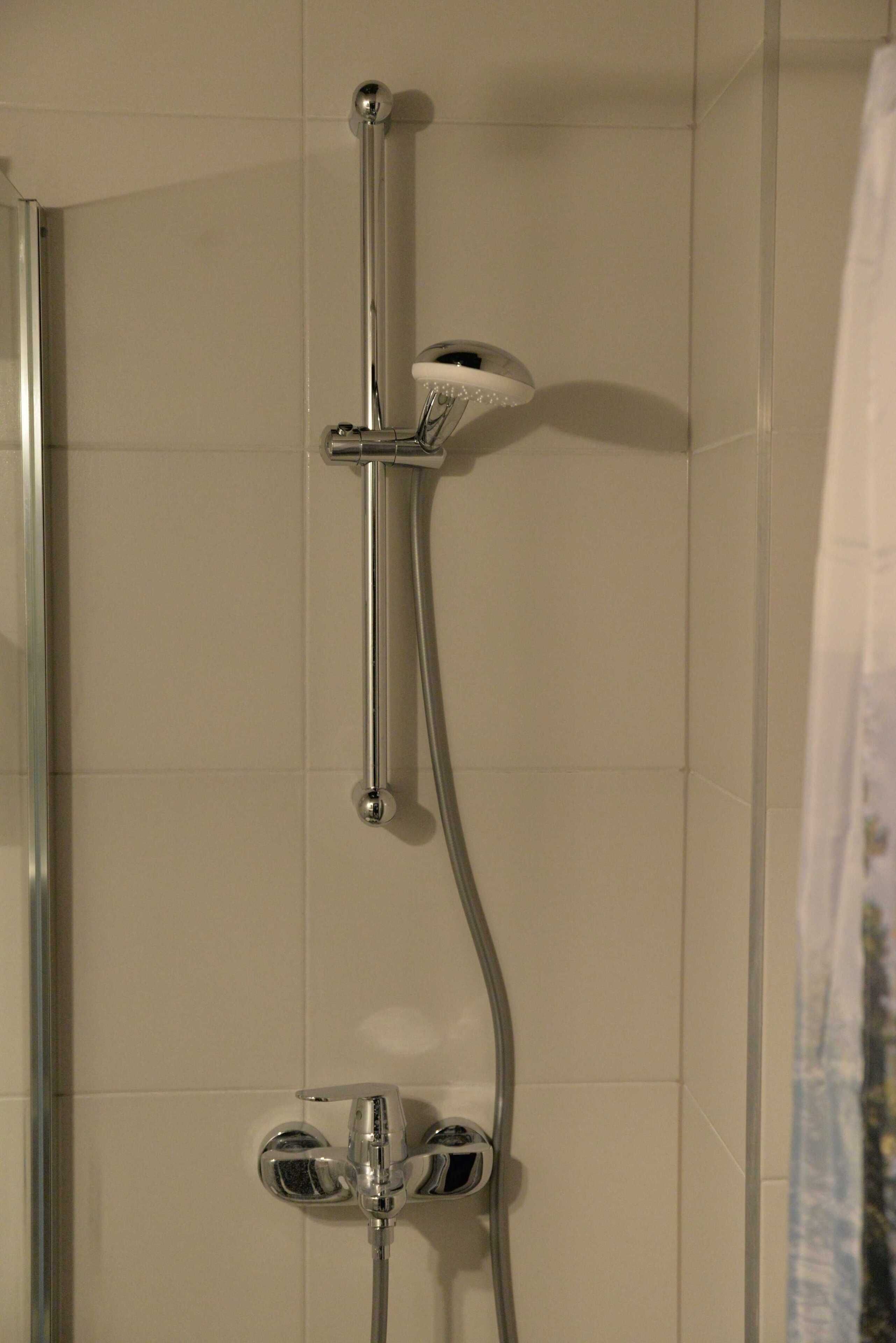 A shower with a chrome faucet and a handheld showerhead mounted on the wall.