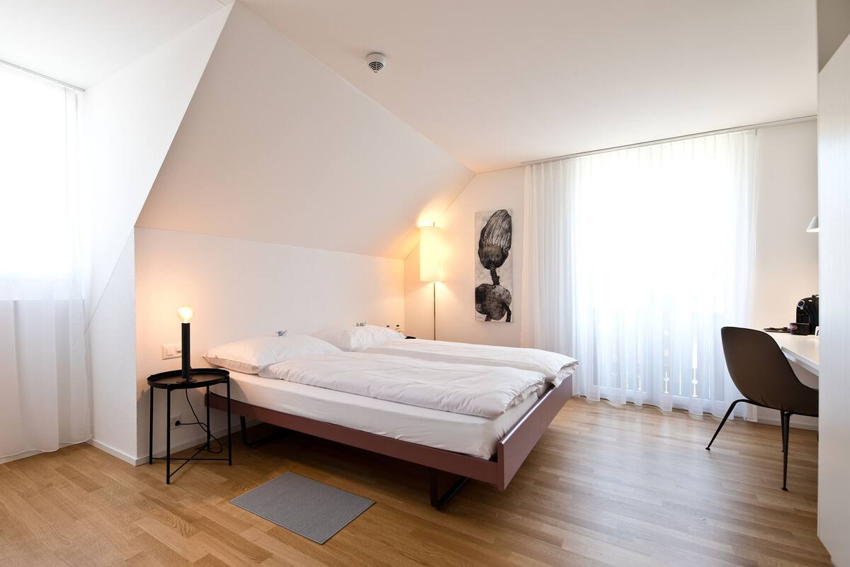 A bedroom with a bed, bedside lamps, a desk, and a chair.
