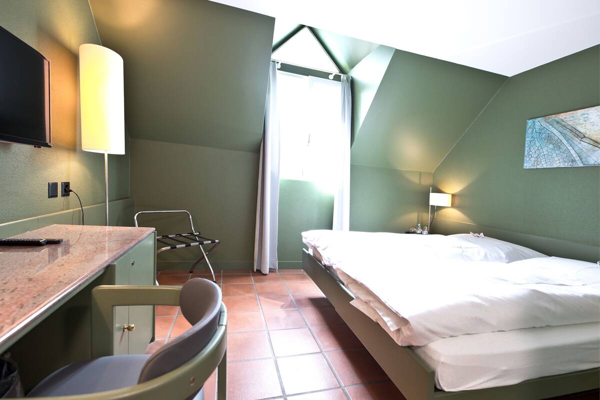 A room with a bed, a desk, a chair, a TV, and a window.