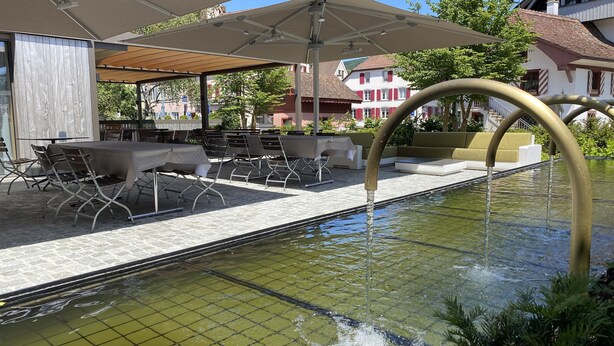 An outdoor dining area with tables and chairs, a covered seating area, and a water feature. - Hotel Restaurant zur Sonne (Sissach)