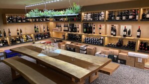 A wine shop with wooden shelves displaying various bottles, a central table with wine glasses, and boxes labeled with brand names. - Hotel Restaurant zur Sonne (Sissach)