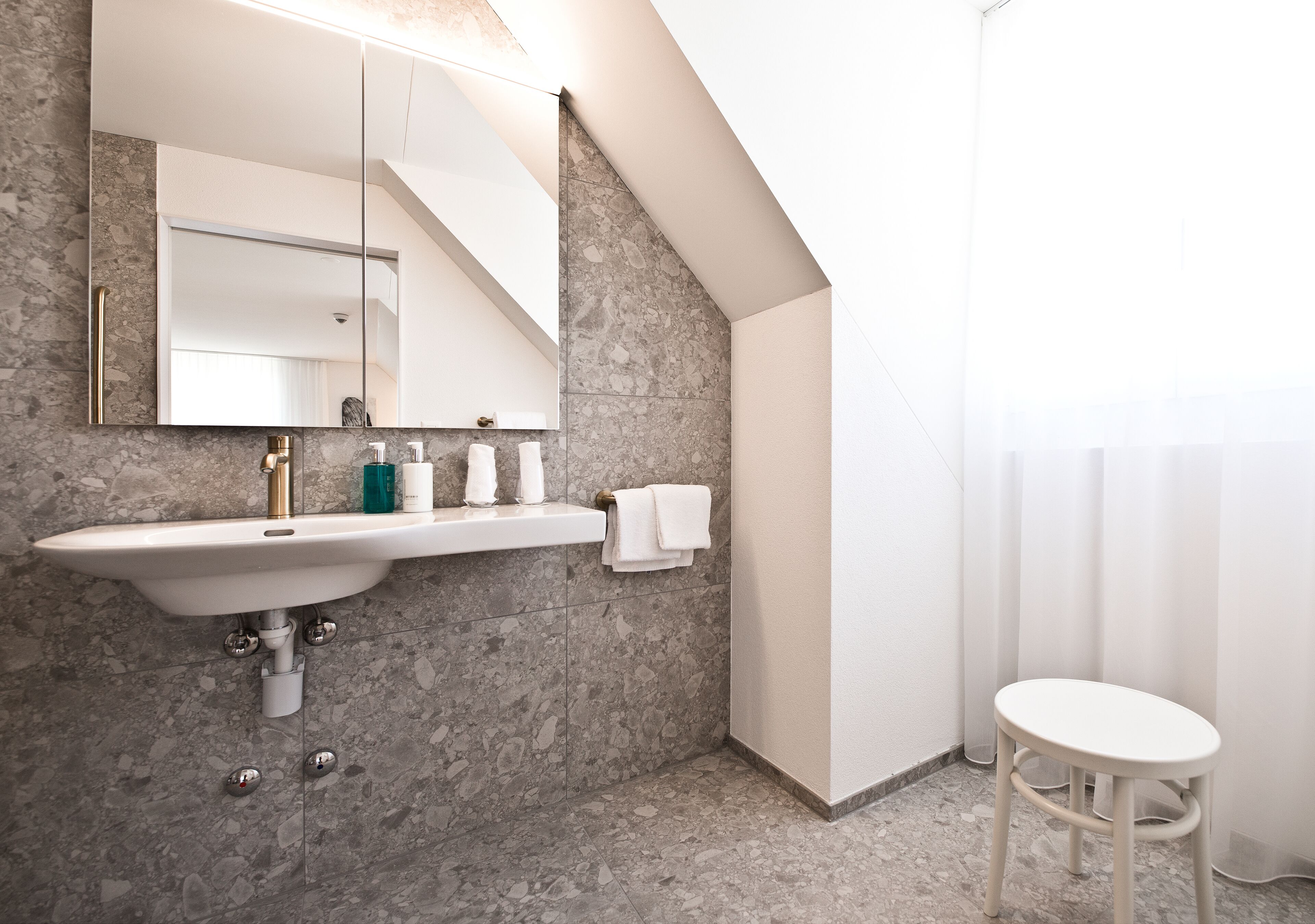 Een moderne badkamer met een marmeren wastafel, een grote spiegel en een witte wastafelunit.