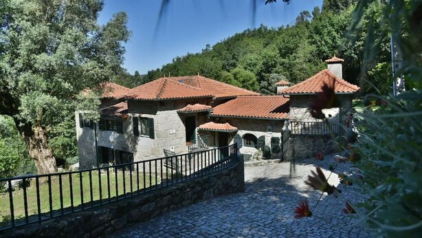 A traditional stone building with red-tiled roofs, surrounded by lush greenery and a cobblestone pathway.