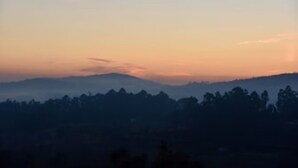 A mountainous landscape during sunset with silhouettes of trees and hills.