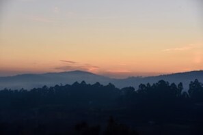A mountainous landscape during sunset with silhouettes of trees and hills.