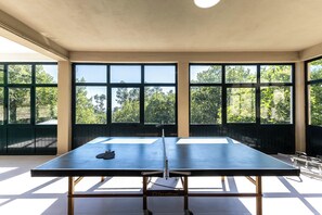 Una mesa de ping pong en una habitación con ventanas amplias y vistas a árboles.