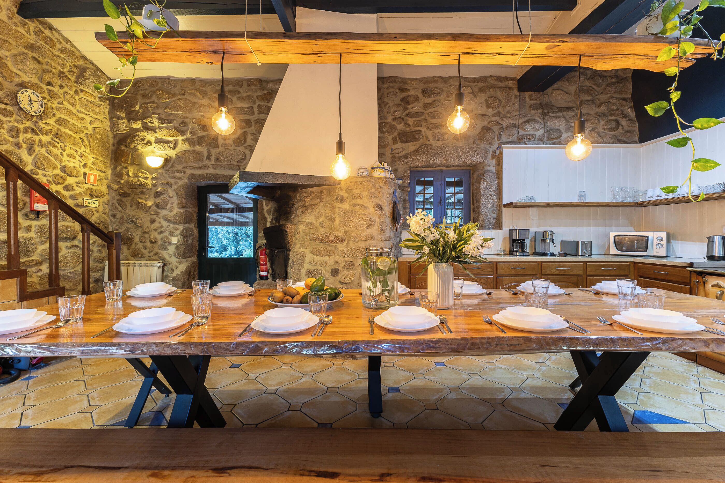 A dining area with a long wooden table set for a meal, stone walls, and hanging light fixtures.