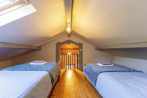 A room with two beds, wooden flooring, a sloped ceiling, and a skylight.