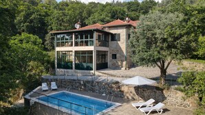 A two-story stone house with a swimming pool and lounge chairs.