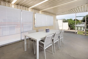Een overdekt terras met een witte tafel en stoelen, een decoratieve schaal en uitzicht op de omgeving.
