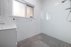 Une salle de bain moderne avec des carreaux blancs, une douche équipée d’un pommeau de douche à main et une fenêtre au-dessus du lavabo.