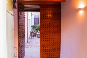 Un couloir étroit, avec une porte en métal ornée de motifs et un luminaire fixé au mur.