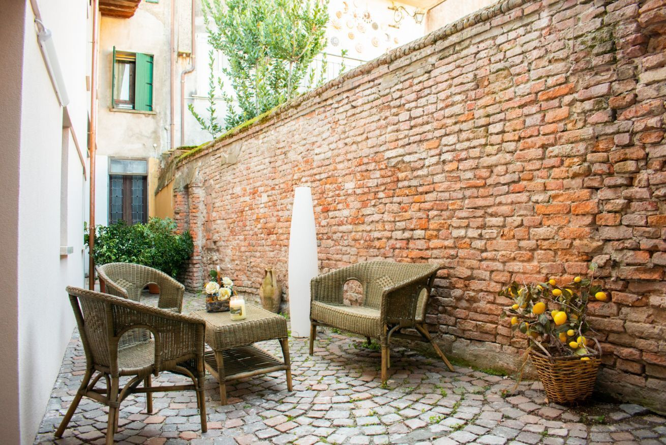 Un patio con mobiliario de mimbre, un muro de ladrillo y una planta en maceta.