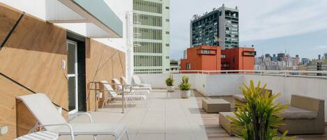 A rooftop terrace with lounge chairs, potted plants, and a cityscape view.