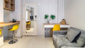 Un espace de vie compact comprenant un coin cuisine, un coin repas avec des chaises jaunes, un canapé gris et un miroir intégré dans la porte.