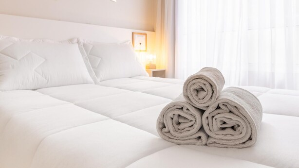 Un lit bien fait, avec du linge de lit blanc et des serviettes enroulées posées sur le côté.