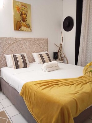 Habitació d'hotel amb llit, almoines, capçalera, obra d'art a la paret, un barret negre i una branca decorativa.