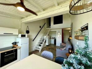 Cocina compacta y moderna con horno empotrado y microondas, una escalera que sube a un altillo, y una zona de estar acogedora con un pequeño árbol de Navidad.